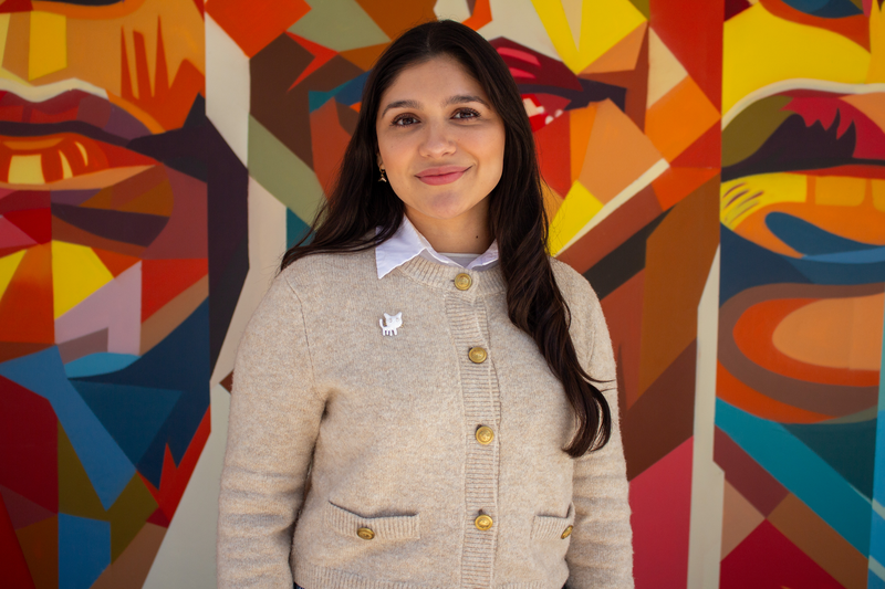 Portrait of Tutor Arely, smiling in front of colorful mural