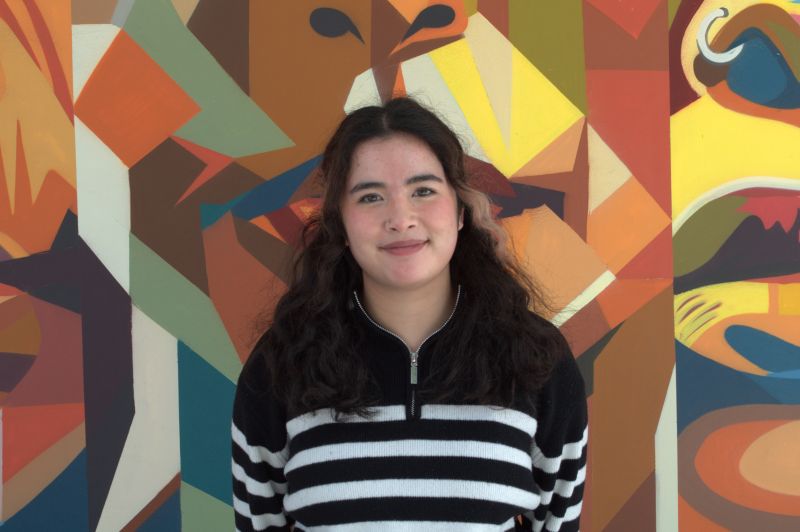 Portrait of Tutor Daisy, smiling in front of colorful mural
