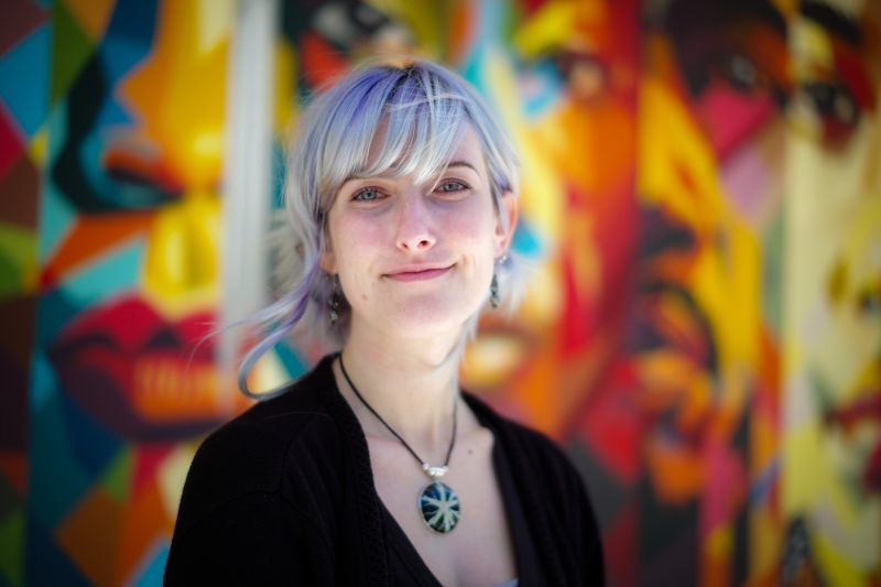 Portrait of Tutor Lacey, smiling in front of colorful mural