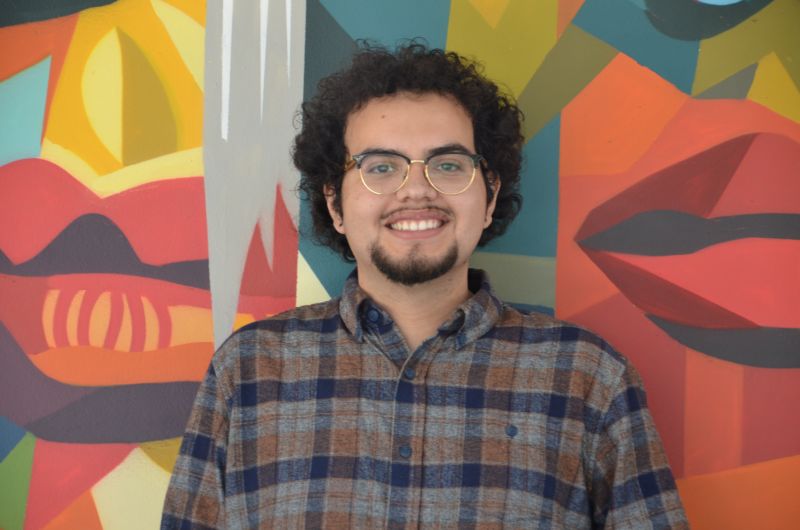 Portrait of tutor Yahir smiling in front of colorful mural