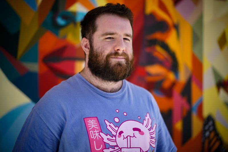 Portrait of tutor Alexander smiling in front of colorful mural