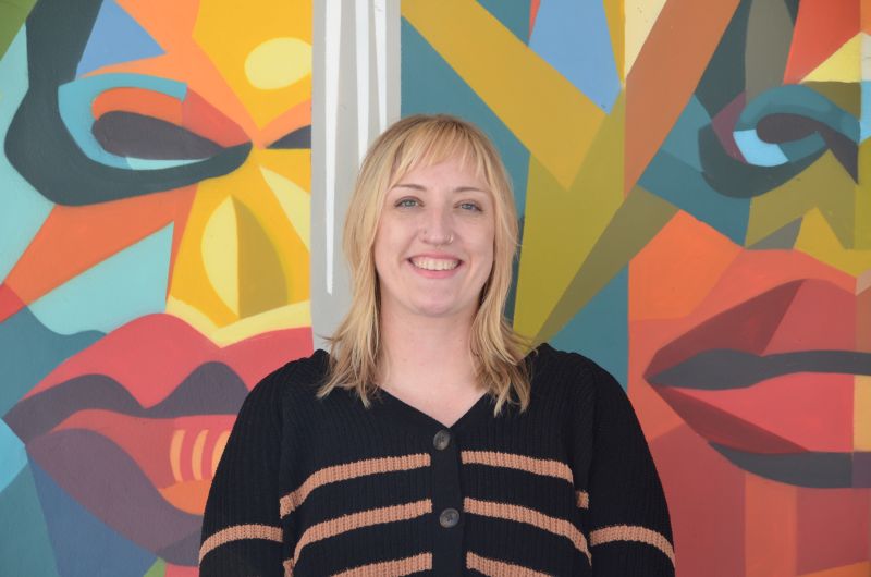 Portrait of tutor Alli smiling in front of colorful mural