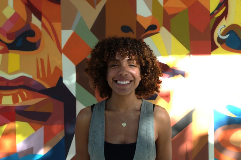 Portrait of tutor Emily smiling in front of colorful mural