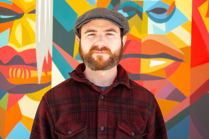 Portrait of tutor Aaron smiling in front of colorful mural