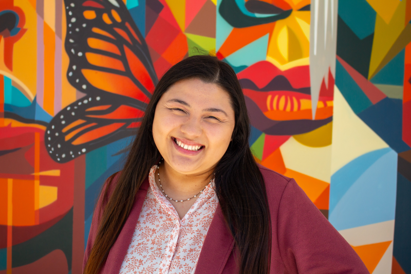 Portrait of tutor Adaniah smiling in front of colorful mural