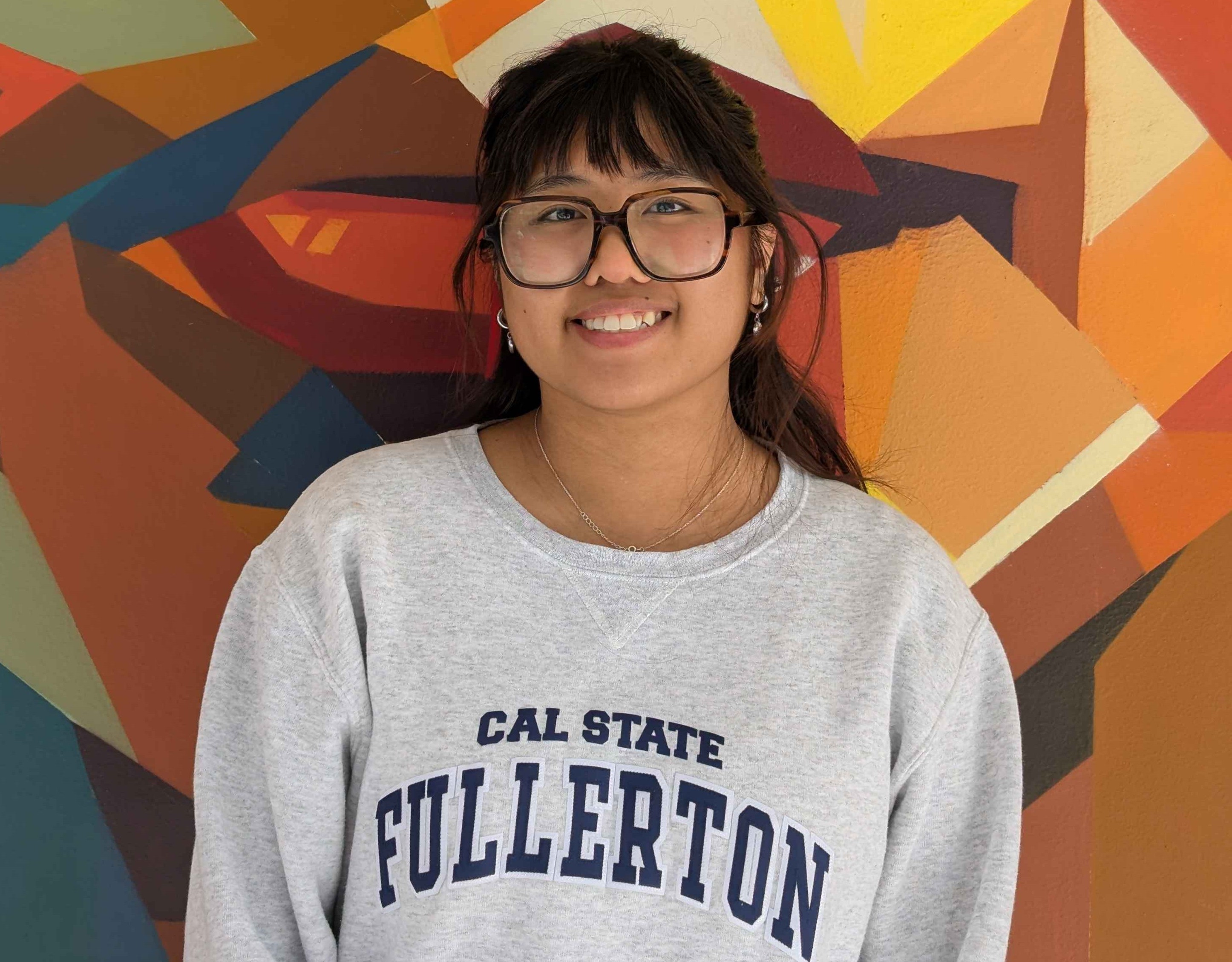 Portrait of tutor Anika smiling in front of colorful mural
