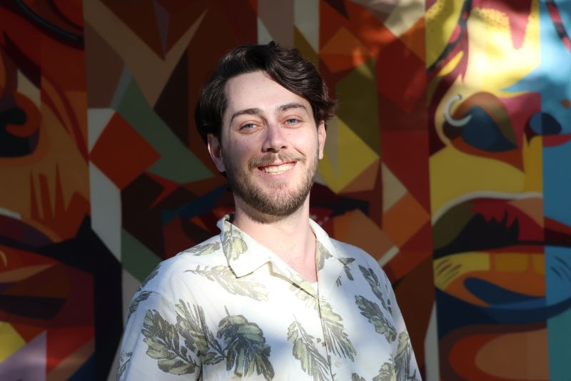 Portrait of tutor Cameron smiling in front of colorful mural