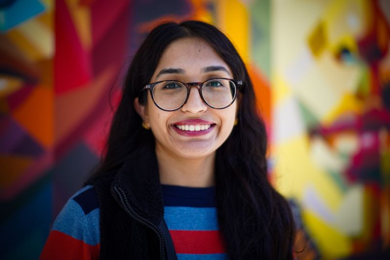 Portrait of tutor Amreen smiling in front of colorful mural