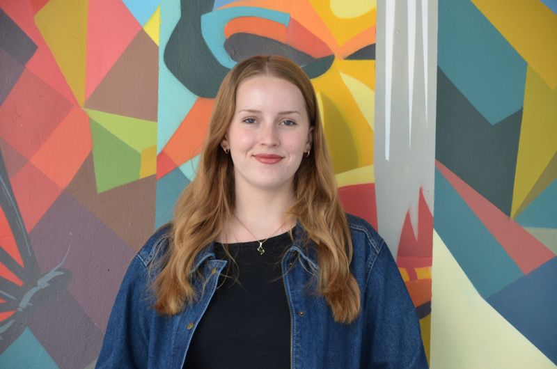 Portrait of tutor Sarah smiling in front of colorful mural