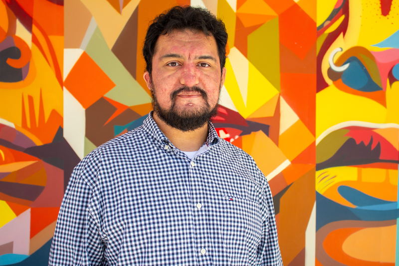 Portrait of tutor Nicholas smiling in front of colorful mural